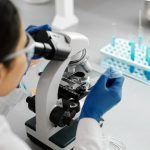 Cientista utiliza um microscópio e um conta-gotas durante pesquisa em laboratório.