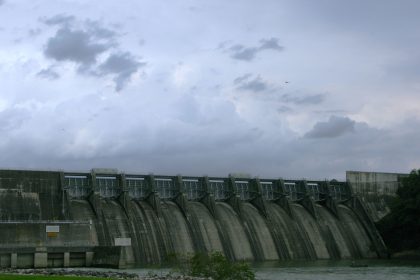 Grande barragem de concreto diante de um céu carregado, destacando sua estrutura e o reservatório de água.