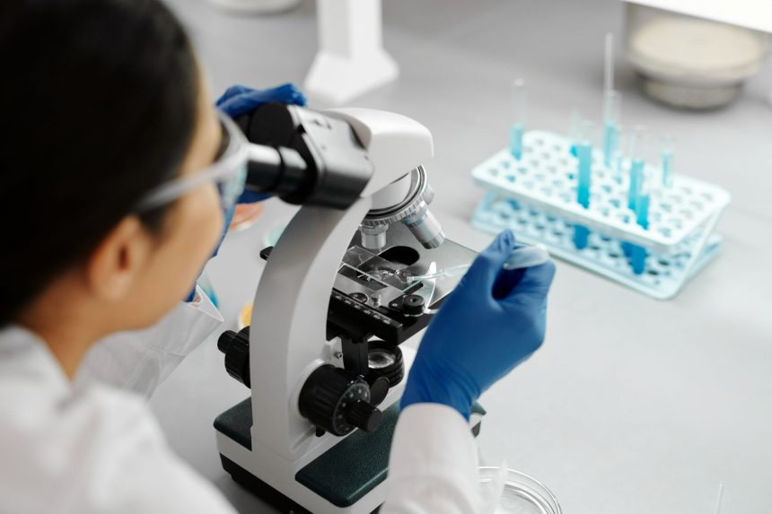 Cientista utiliza um microscópio e um conta-gotas durante pesquisa em laboratório.
